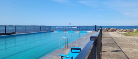 A clear blue pool with a metal railing, a concrete deck, and a view of the sea.