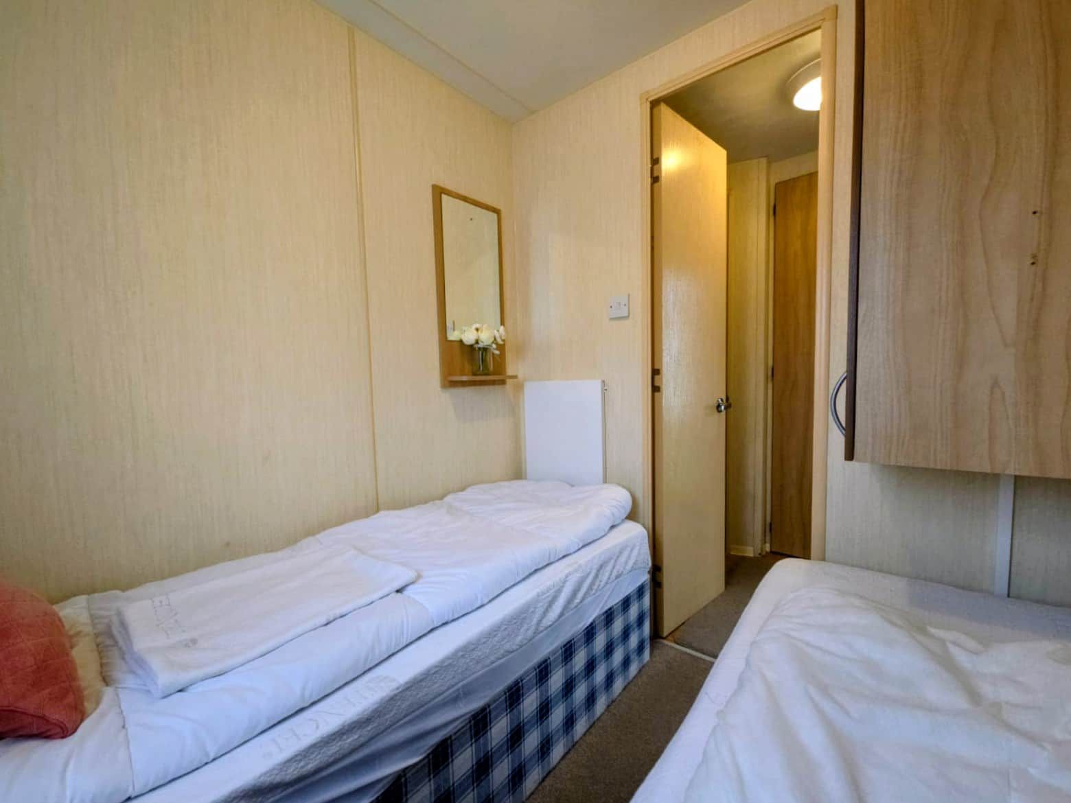 Une chambre avec deux lits, une armoire en bois, un miroir et une porte donnant sur une autre pièce.