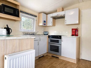 A compact kitchen with a microwave, stove, and a fire extinguisher. - The Retreat Anchorage – 8-Berth Caravan (Rhyl)