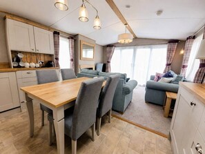 A modern kitchen with a dining table and chairs, a sofa, and a small table with a lamp. - The Retreat Ambleside – Pet Friendly (Prestatyn)