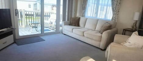 Una sala de estar con sofá, sillón, televisión y puerta corrediza de vidrio que da a un espacio exterior.