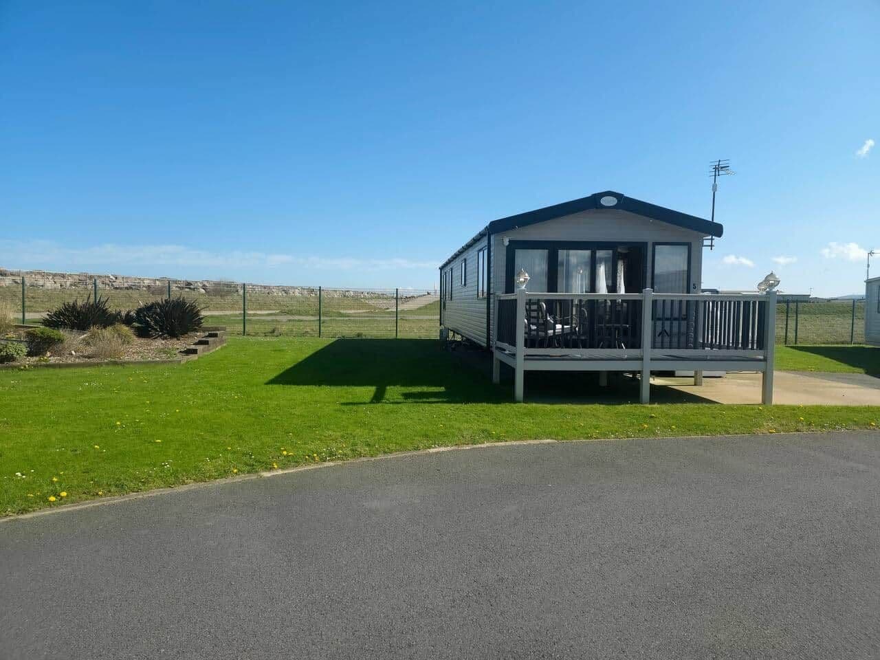 A small, single-story building with a balcony, situated on a grassy area with a clear sky.