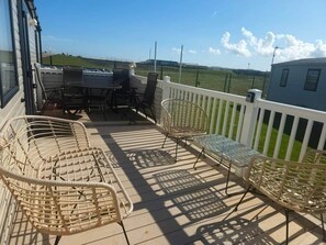 Eine überdachte Terrasse im Freien mit Korbmöbeln, einem weißen Geländer und Blick auf die Landschaft.