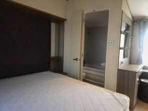 Quarto com cama, porta para um banheiro e uma mesinha.
