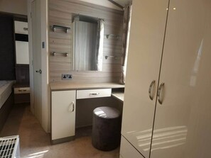 Quarto compacto com cama, mesa de cabeceira, guarda-roupa e espelho.