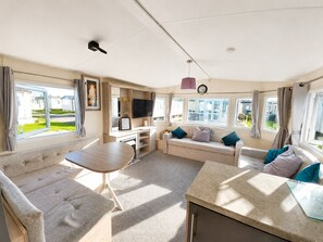 Ein Caravan-Innenraum mit einer Sitzecke, einem Fernseher und einem Fenster mit Blick auf eine Wohngegend.