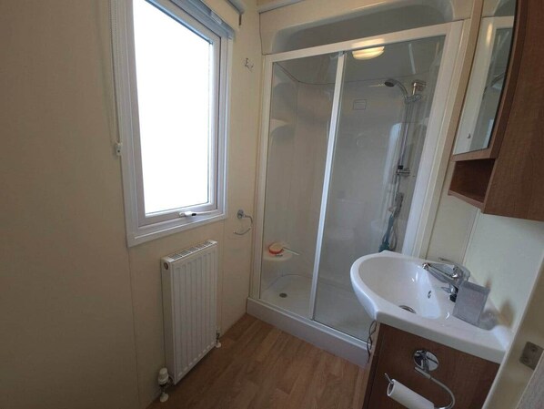Un baño con cabina de ducha de vidrio, un lavamanos blanco y un ventanal que proporciona luz natural.