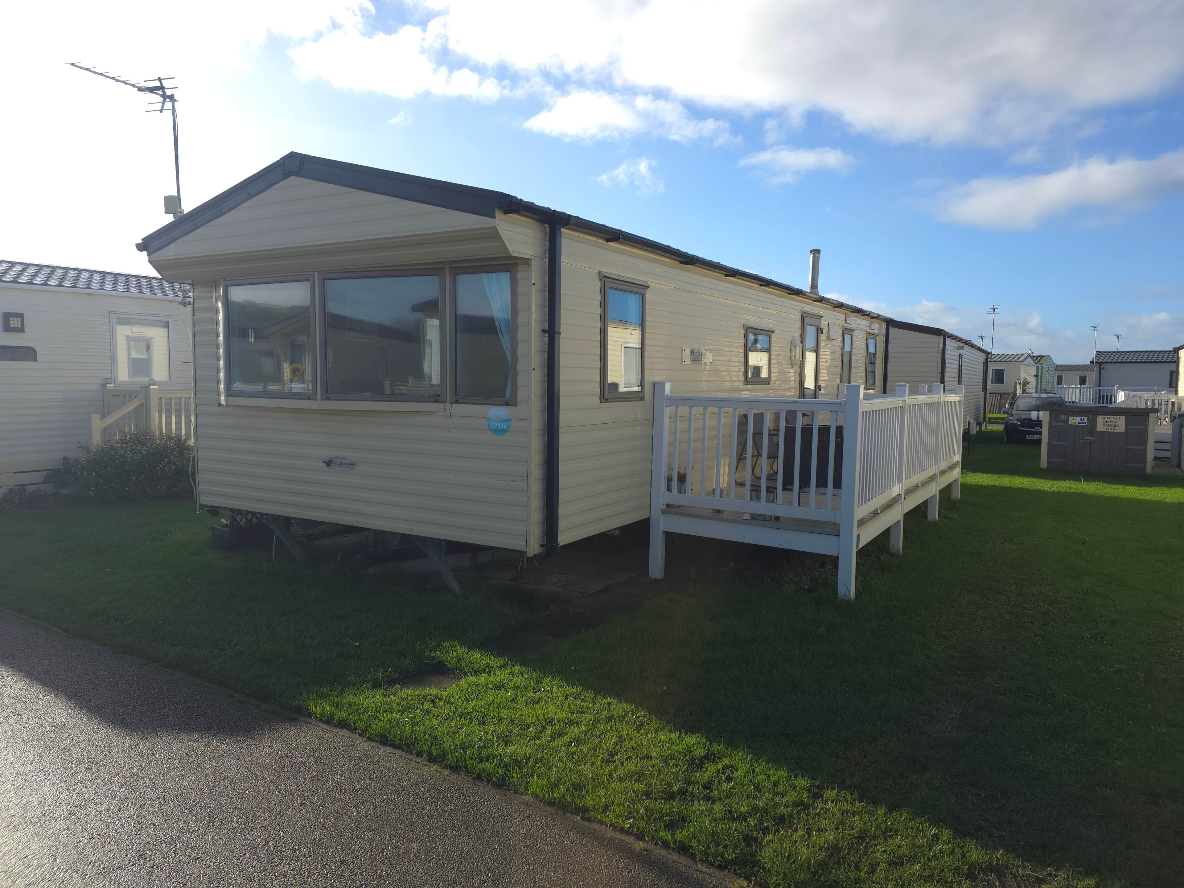 A mobile home with a fenced deck, a chimney, and a satellite dish.
