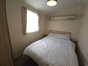 A single bed with a wooden headboard in a room with a window and a wall-mounted shelf. - The Retreat Mistral | Towyn Bay Rhyl (No Pets) (Towyn)