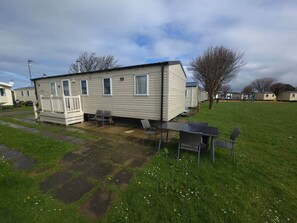 A mobile home with a patio area, a small table, and chairs. - The Retreat Mistral | Towyn Bay Rhyl (No Pets) (Towyn)