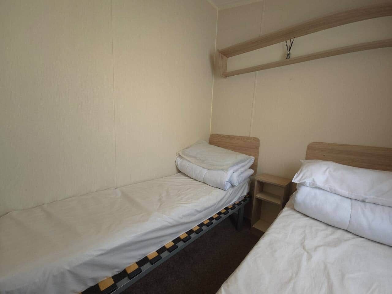 A small, single-room accommodation with two single beds, a wooden headboard, and a simple bedside table.
