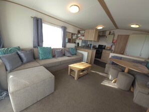 A compact living space with a sofa, a small wooden table, and a kitchenette area. - The Retreat Oakley - Marine Holiday Park Rhyl (Rhyl)