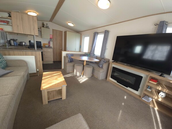 Un espacio habitable compacto con kitchenette, un sofá, un televisor y una pequeña mesa de comedor.