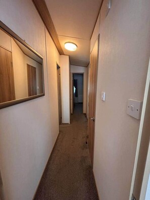 Un pasillo estrecho con suelos alfombrados, puertas de madera y un aplique en el techo.