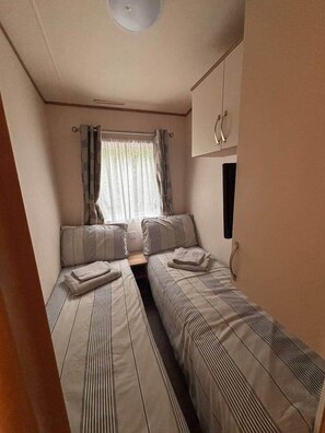 Een kleine kamer met twee eenpersoonsbedden, een raam met gordijnen en een kastje.