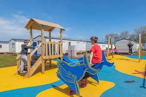 Kinder spielen auf einem Spielplatz mit einer hölzernen Kletterkonstruktion und einer blauen Rutsche.