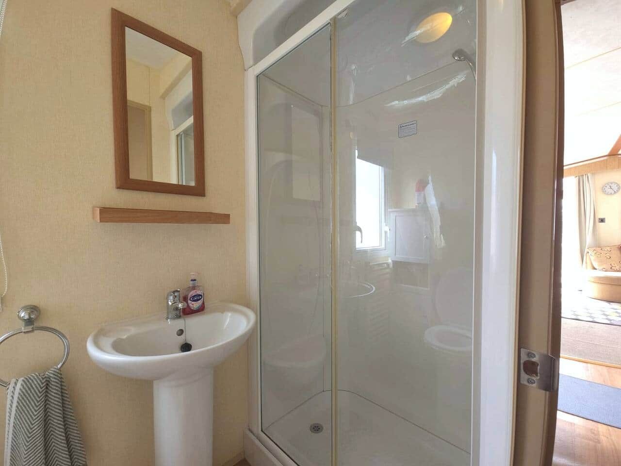 Ein Badezimmer mit Duschkabine aus Glas, Waschbecken und Spiegel.