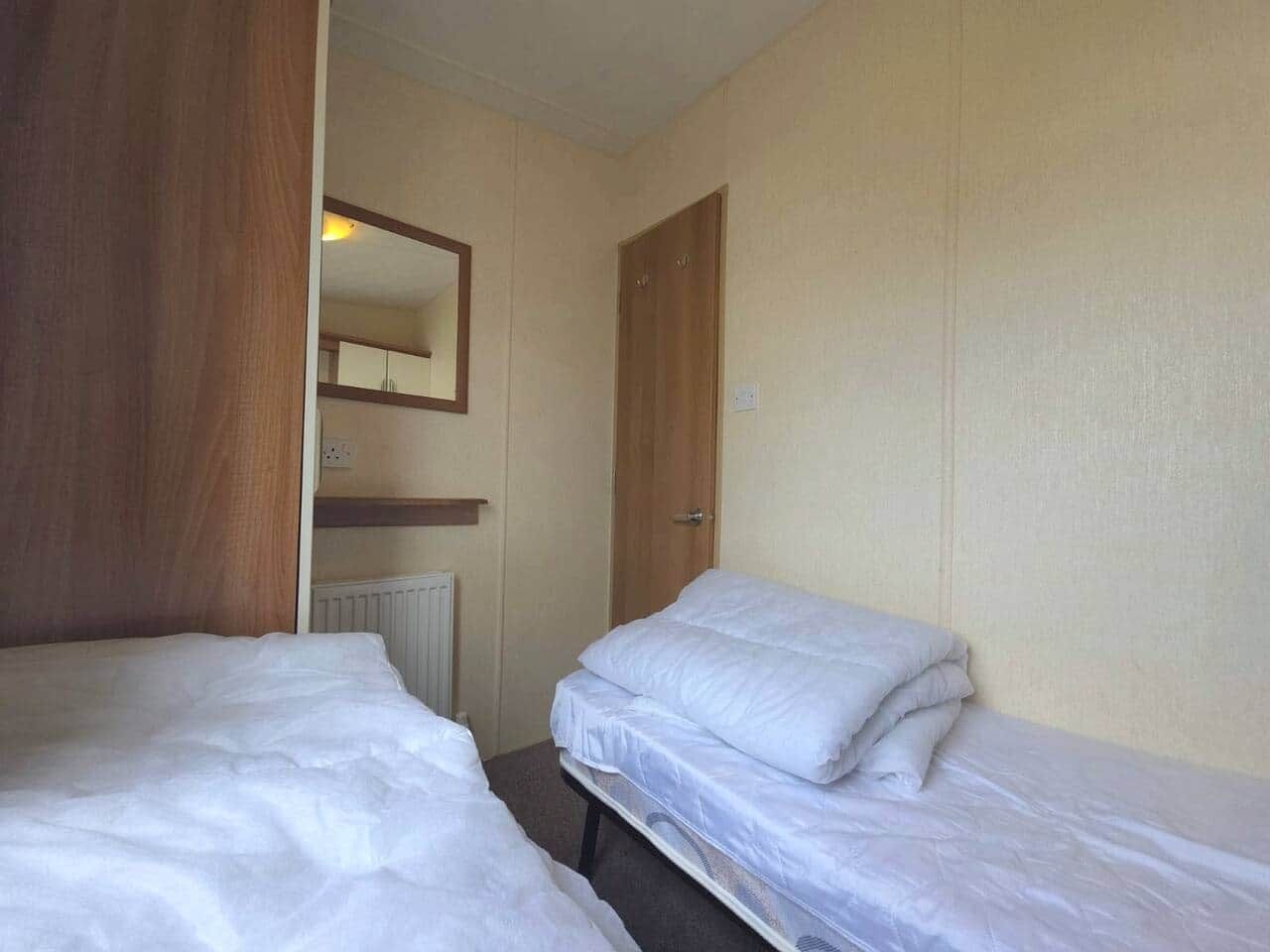 A room with two single beds, a wooden wardrobe, a radiator, and a mirror on the wall.