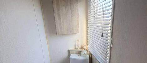 Un baño pequeño y funcional con inodoro, un mueble de pared encima, un radiador y una ventana con persianas.