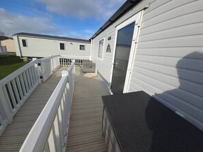 Une terrasse qui mène à une maison mobile à l’extérieur blanc et au toit noir.