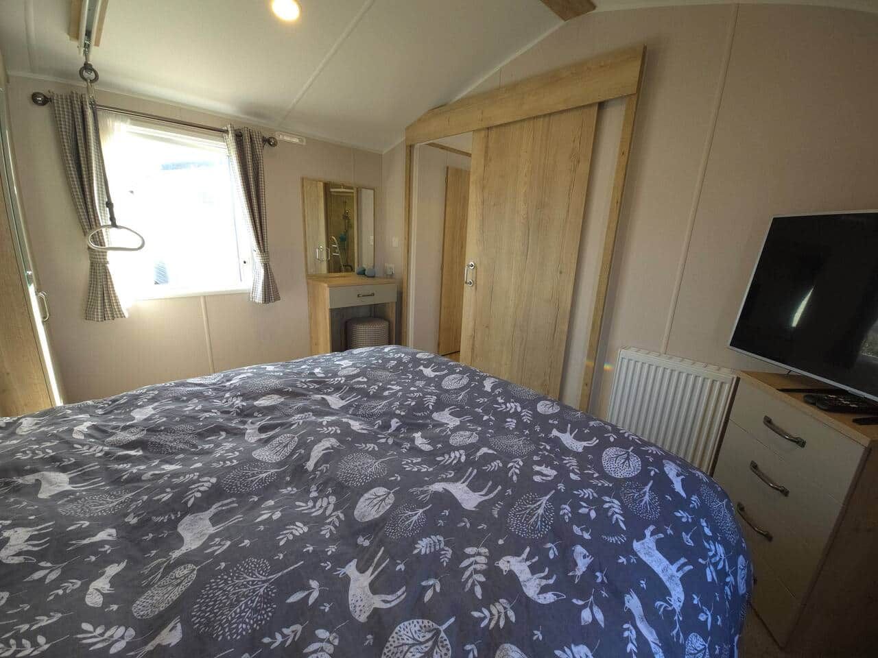 Une chambre à coucher comprenant un lit, une télévision, une armoire et une fenêtre avec des rideaux.
