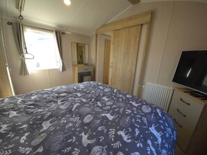 A bedroom with a bed, a television, a wardrobe, and a window with curtains. - The Retreat Haven - Wheelchair-Friendly Caravan (Prestatyn)