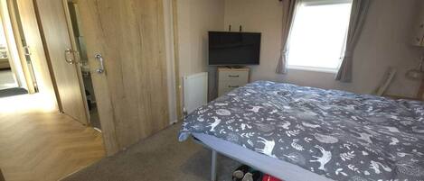 A bedroom with a bed, a television, a radiator, and a window with curtains.