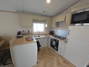 A compact kitchen with a gas stove, oven, microwave, and a sink. - The Retreat Haven - Wheelchair-Friendly Caravan (Prestatyn)