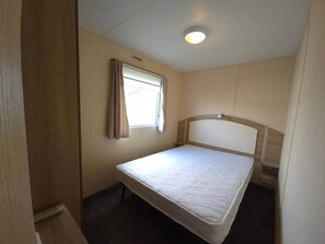 Ein Einzelbett in einem Zimmer mit Fenster, Deckenleuchte und Holzwänden.