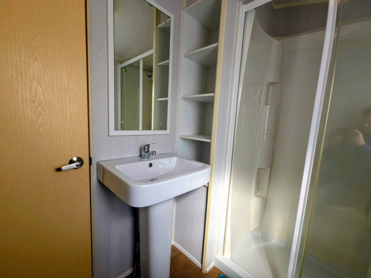 Un baño con lavamanos blanco, un espejo y cabina de ducha.