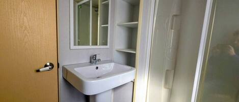 Un baño con lavamanos blanco, un espejo y cabina de ducha.