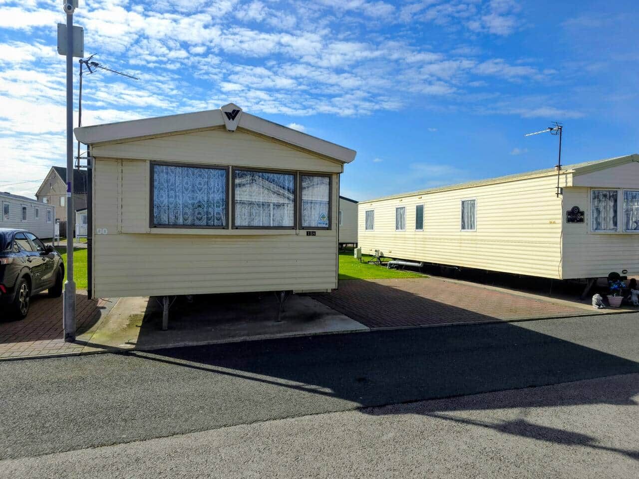 En campingvogn med en lille veranda, en bil foran og en klar himmel.
