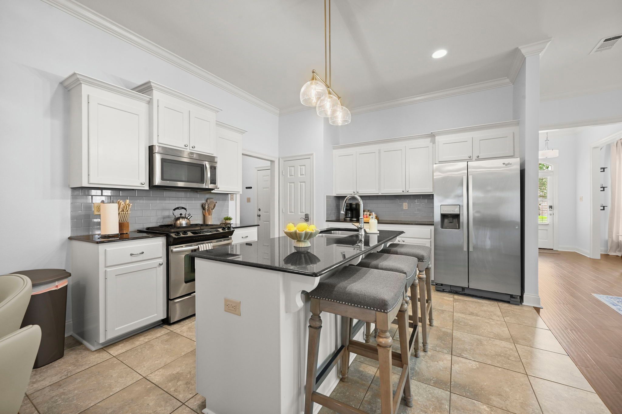 A modern kitchen with white cabinetry, stainless steel appliances, and a central island with bar stools.