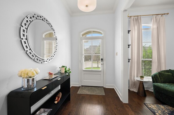 A hallway with a black console, a round mirror, a white door with a window, and a green sofa.