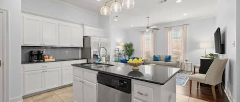 Una cocina moderna con armarios blancos, una isla central, electrodomésticos de acero inoxidable y una zona de comedor con sofá y sillas.