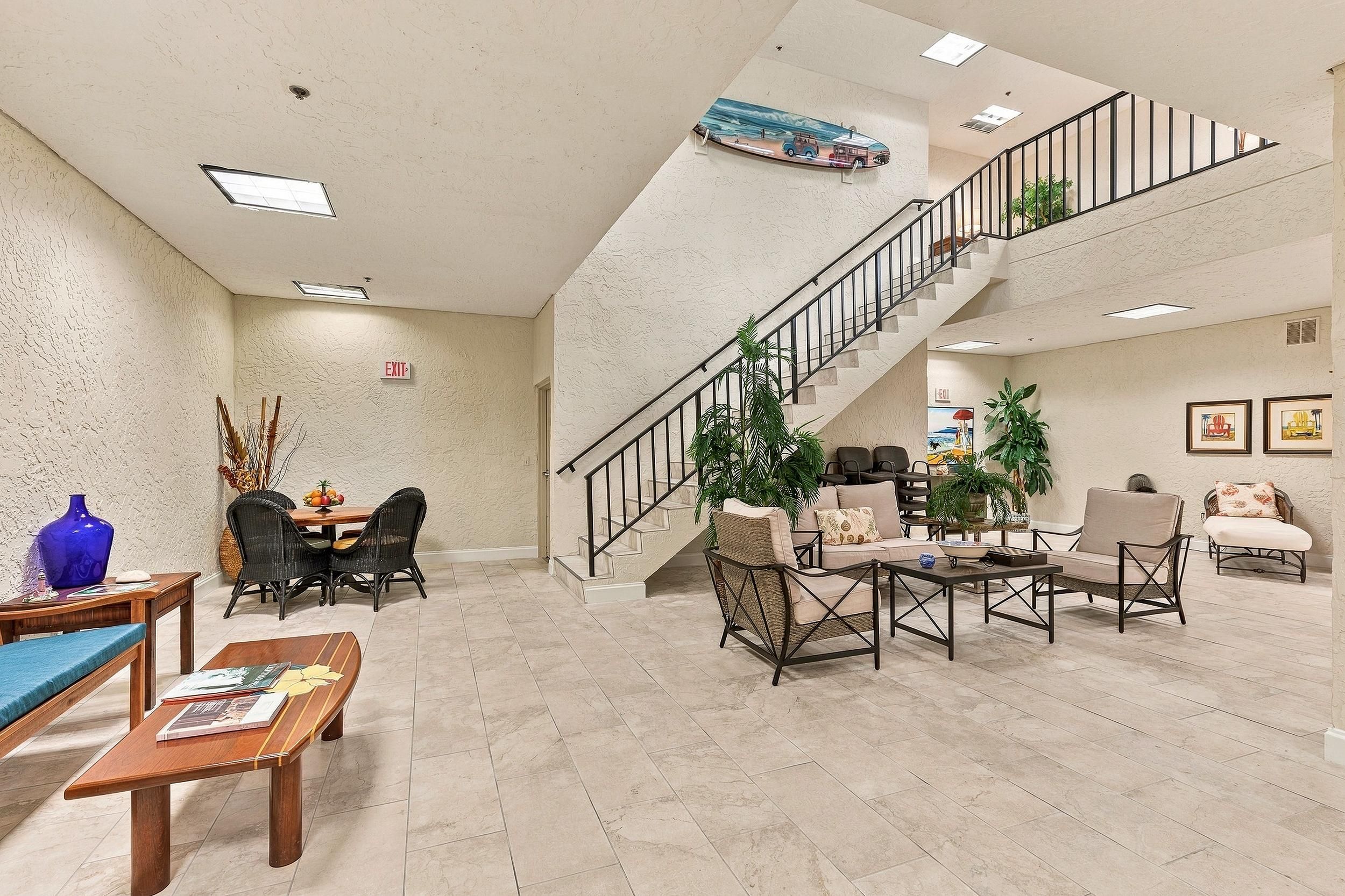A spacious lobby with a high ceiling, a staircase, and a dining area with wicker furniture.