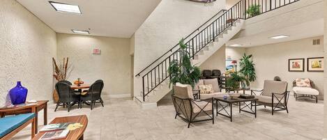 A spacious lobby with a high ceiling, a staircase, and a dining area with wicker furniture.