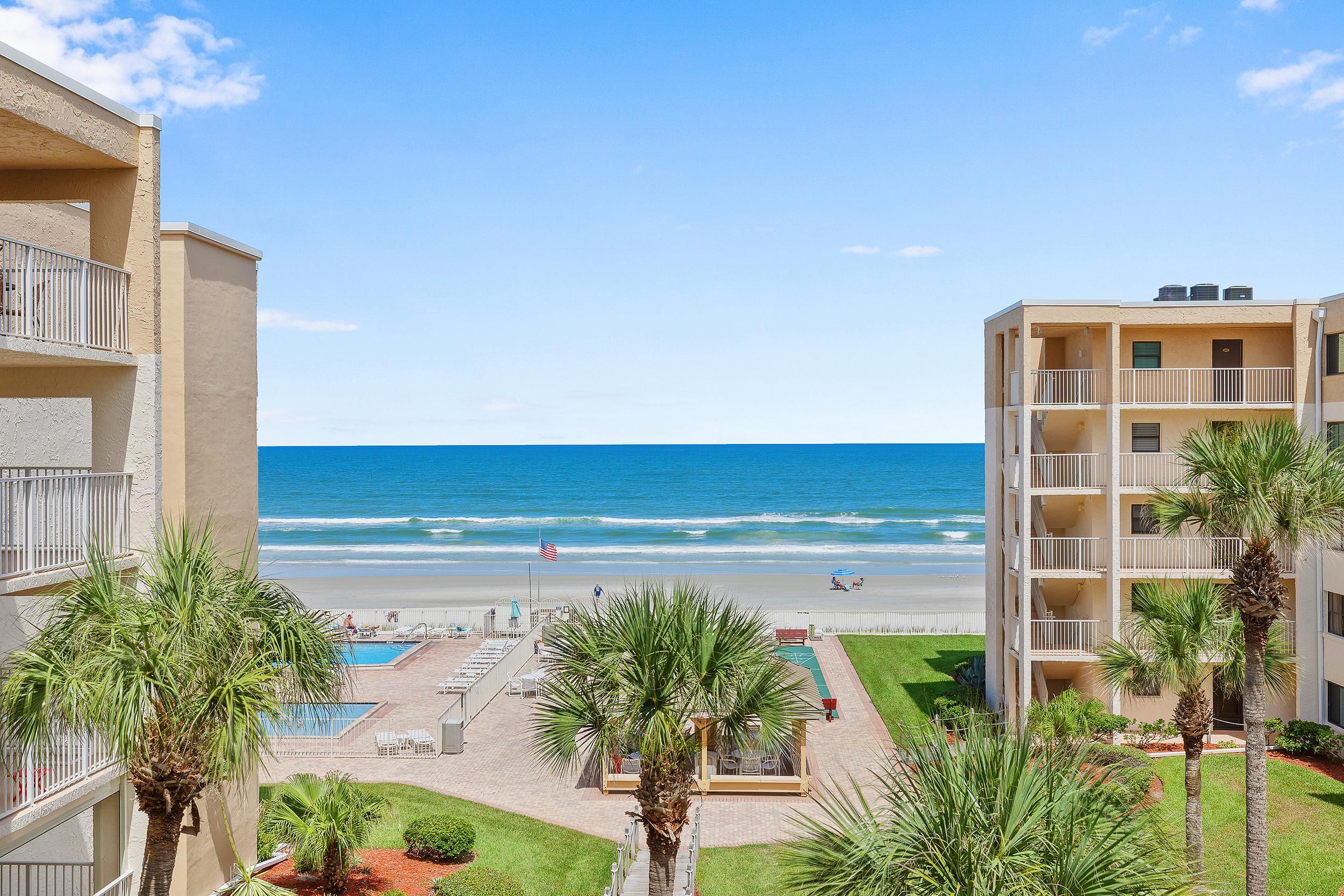 Un hotel fronte spiaggia con piscina, palme e vista sull'oceano.