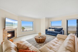 A spacious living room with a fireplace, a large sofa, a coffee table, and a television. - Seascape Towers 222 (New Smyrna Beach)