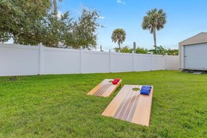 Patio trasero con valla blanca, dos mesas de picnic de madera con cojines y un garaje.