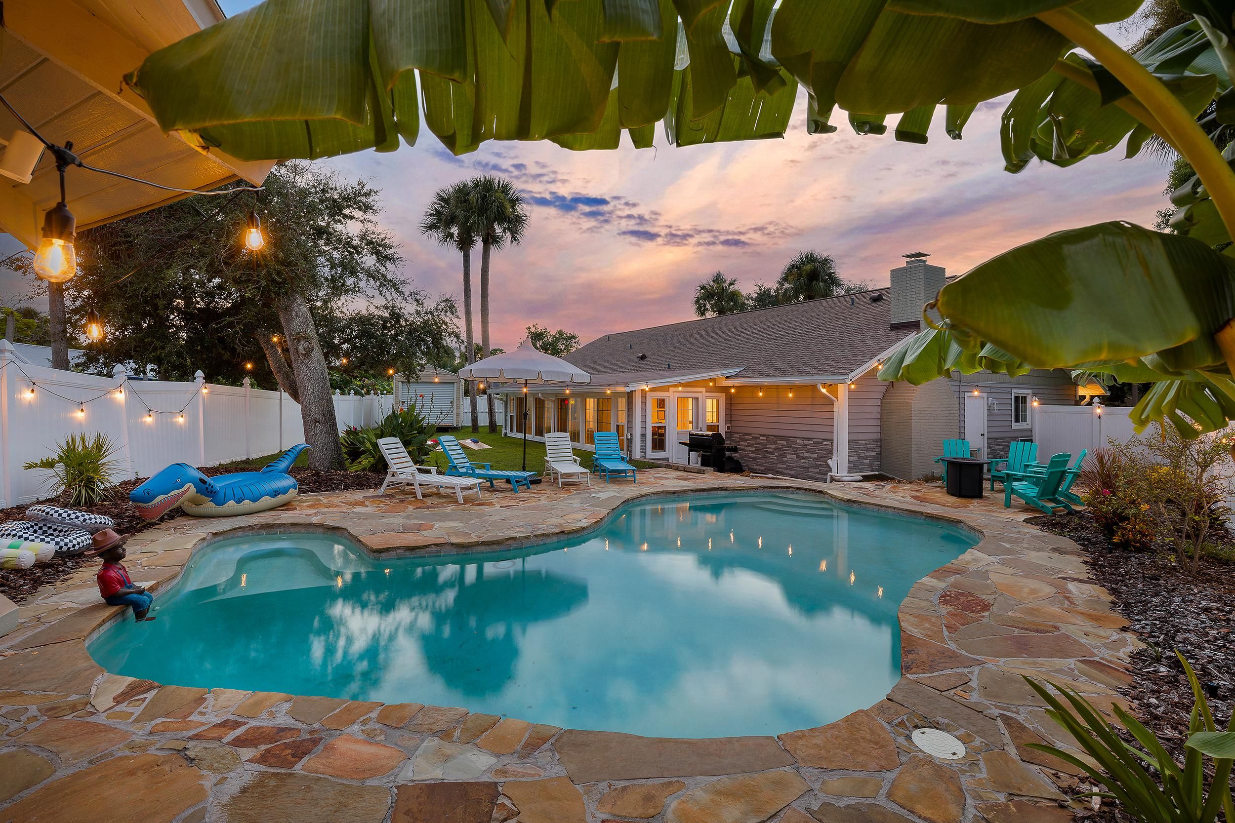 A backyard with a swimming pool, lounge chairs, and a patio area.