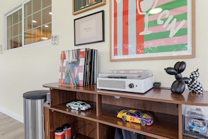 Una habitación con un escritorio de madera, un equipo de sonido, un cartel enmarcado, un control remoto y un coche de juguete.