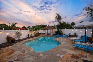 A swimming pool with stone tiles, surrounded by lounge chairs and a pergola. - The Checkered Palm (Port Orange)