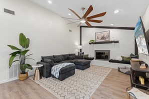 A modern living room with a sectional sofa, a ceiling fan, a fireplace, and a mounted TV. - The Checkered Palm (Port Orange)