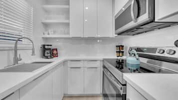 Una cucina moderna con mobili bianchi, piano cottura in acciaio inossidabile, forno a microonde e bollitore.