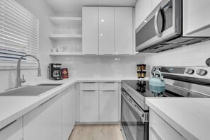 A modern kitchen with white cabinetry, a stainless steel range, a microwave, and a kettle.