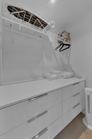 Una habitación blanca con una cama, una mesita de noche, una lámpara y un radiador.