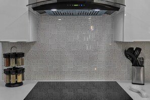 A modern kitchen with a patterned backsplash, a stainless steel range hood, and a spice rack with black containers.