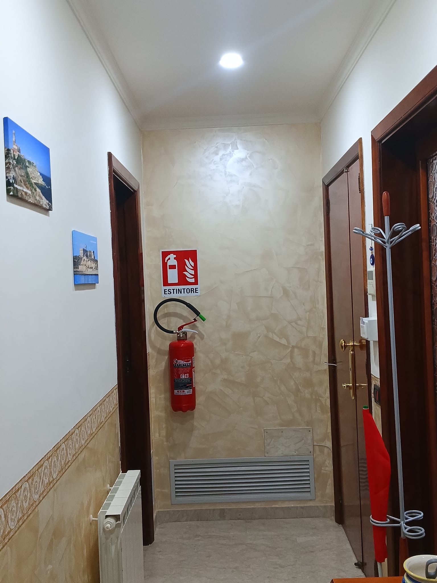 A hallway with a fire extinguisher mounted on the wall, a radiator, and a door with a coat rack.