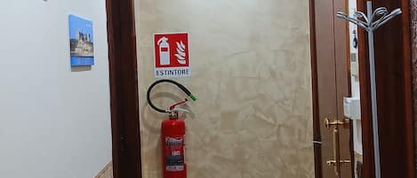 A hallway with a fire extinguisher mounted on the wall, a radiator, and a door with a coat rack.
